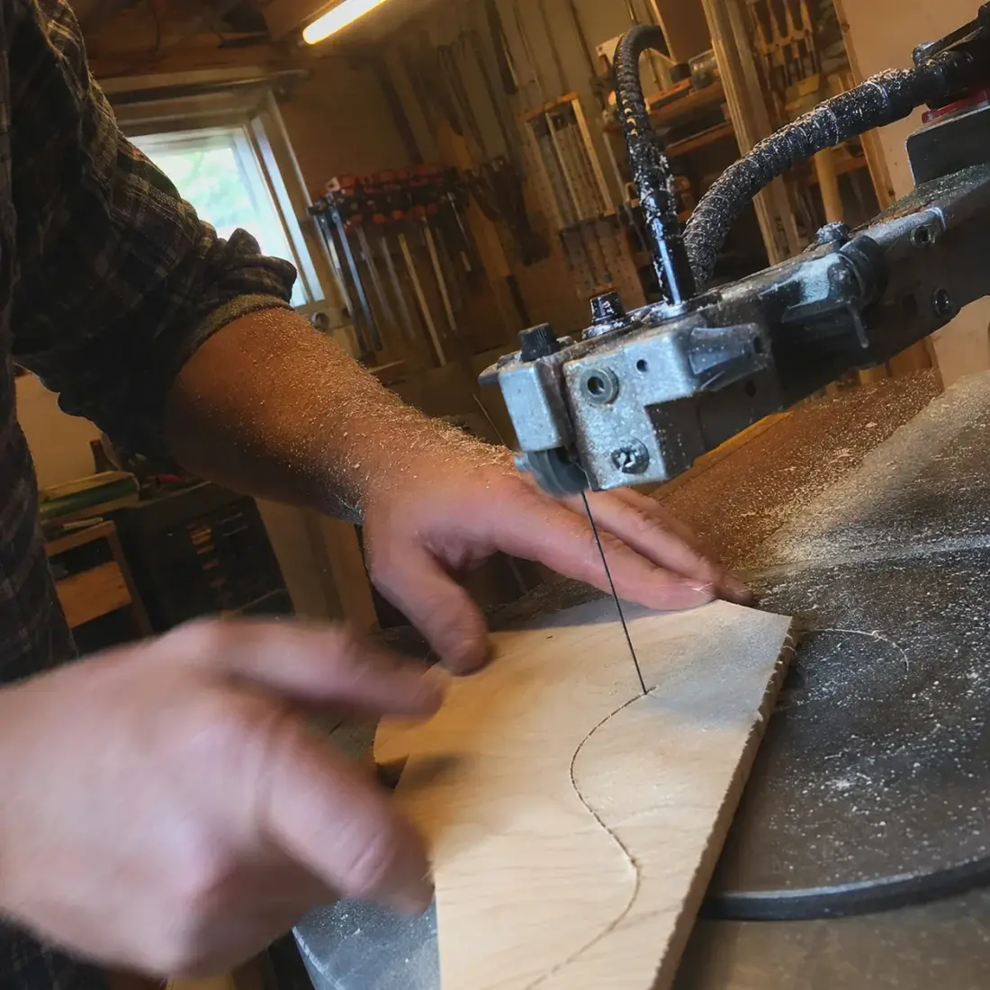 Scroll sawyer guiding a maple board through the blade in a dust-filled workshop